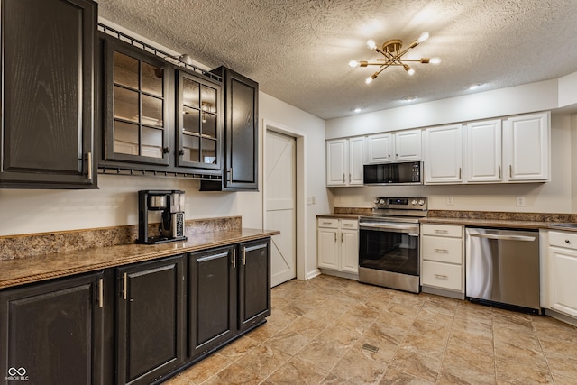 kitchen with stainless steel appliances, glass insert cabinets, dark countertops, and white cabinets