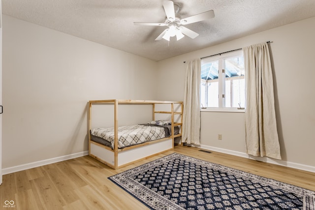 bedroom with visible vents, a textured ceiling, baseboards, and wood finished floors