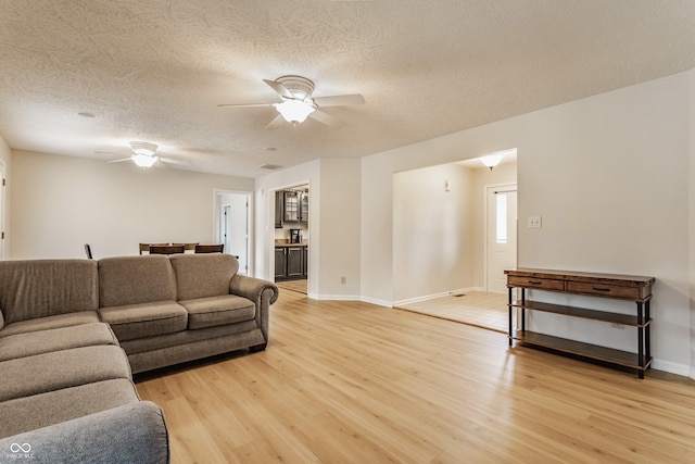 living area with baseboards, ceiling fan, a textured ceiling, and light wood-style floors