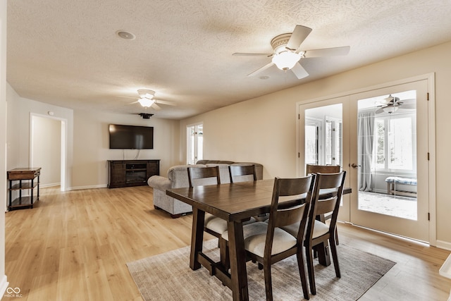 dining space with a ceiling fan, baseboards, french doors, light wood-style floors, and a textured ceiling