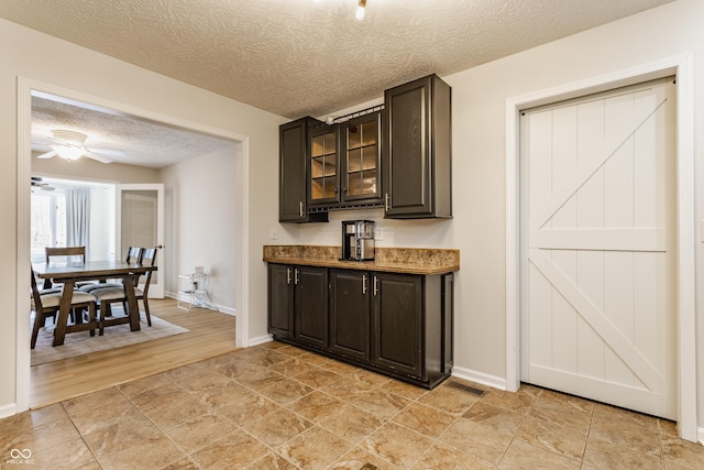 bar featuring visible vents, a textured ceiling, baseboards, and a ceiling fan