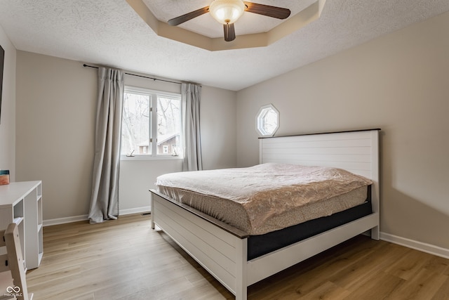 bedroom featuring light wood finished floors, a textured ceiling, and baseboards