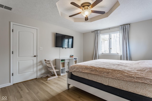 bedroom with a tray ceiling, light wood-style floors, visible vents, and a textured ceiling