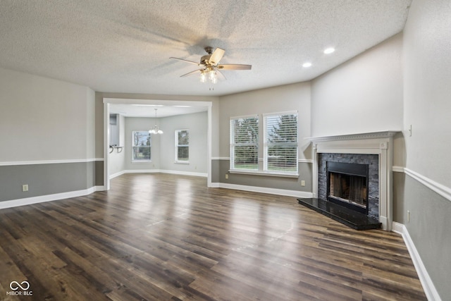 unfurnished living room featuring a textured ceiling, ceiling fan with notable chandelier, a fireplace, and dark hardwood / wood-style flooring