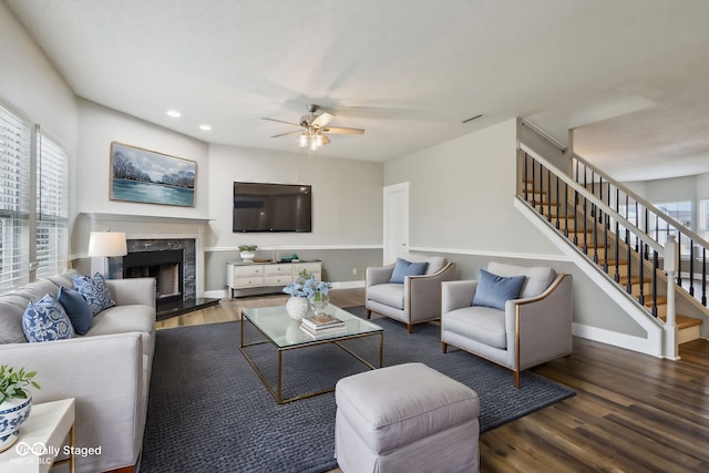 living room featuring dark wood-type flooring, ceiling fan, and a premium fireplace