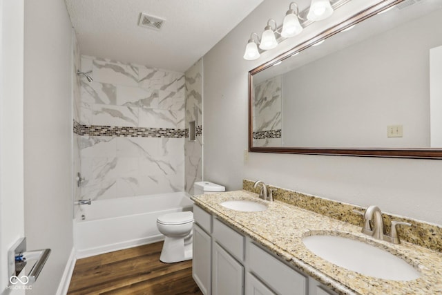 full bathroom featuring wood-type flooring, tiled shower / bath combo, vanity, toilet, and a textured ceiling