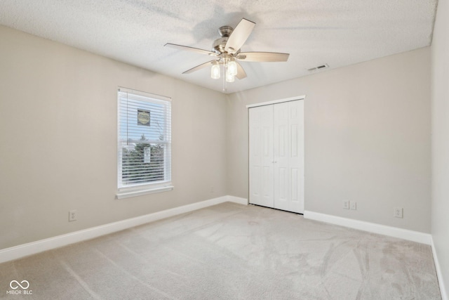 unfurnished bedroom with light carpet, ceiling fan, a closet, and a textured ceiling