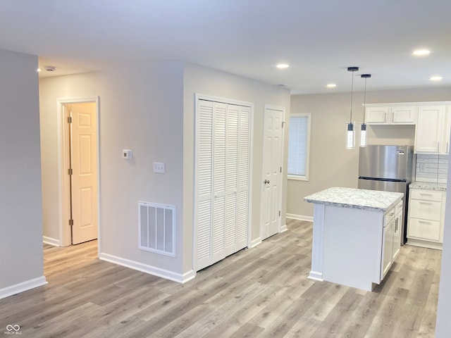 kitchen featuring pendant lighting, light hardwood / wood-style flooring, stainless steel refrigerator, white cabinetry, and a kitchen island