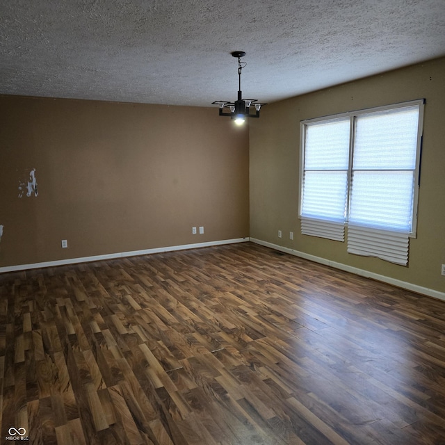 empty room featuring dark hardwood / wood-style flooring, a notable chandelier, and a textured ceiling