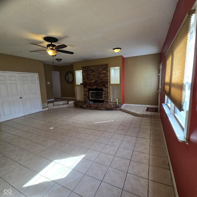 unfurnished living room featuring light tile patterned flooring, ceiling fan, a brick fireplace, and a textured ceiling