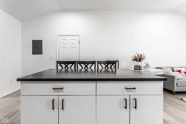 kitchen with white cabinetry, vaulted ceiling, electric panel, and light hardwood / wood-style flooring