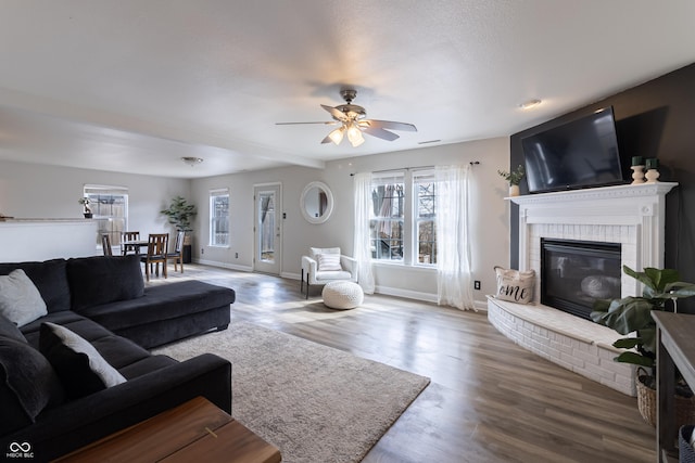 living area with a brick fireplace, a healthy amount of sunlight, baseboards, and wood finished floors