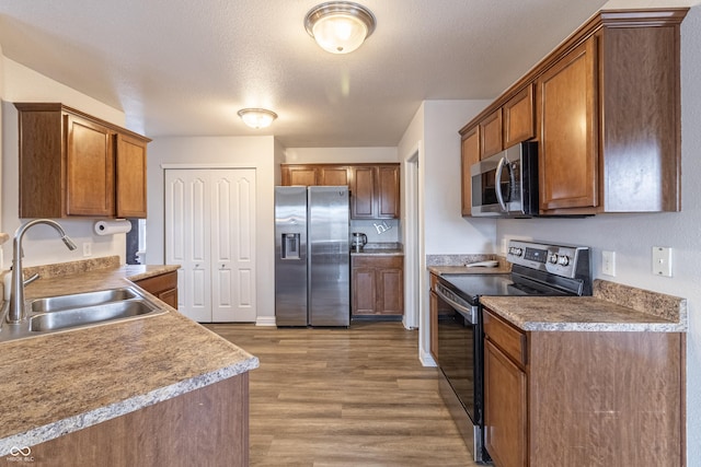 kitchen with brown cabinets, stainless steel appliances, a sink, and wood finished floors