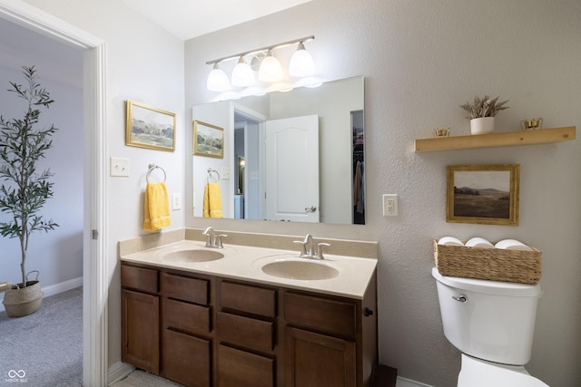 bathroom with double vanity, baseboards, toilet, and a sink