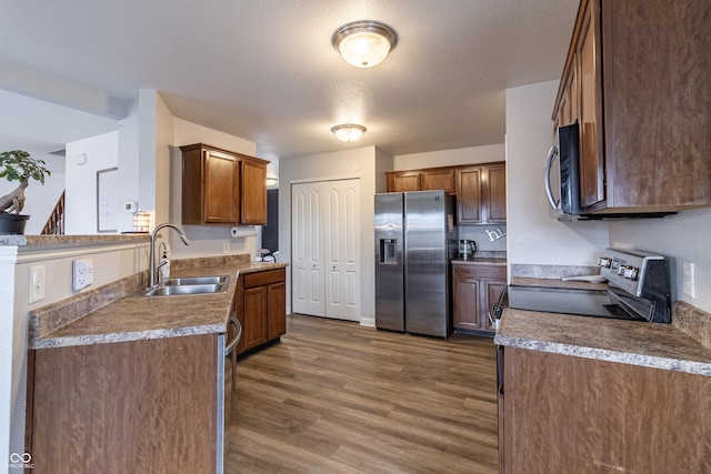 kitchen with a textured ceiling, appliances with stainless steel finishes, dark wood-style flooring, and a sink