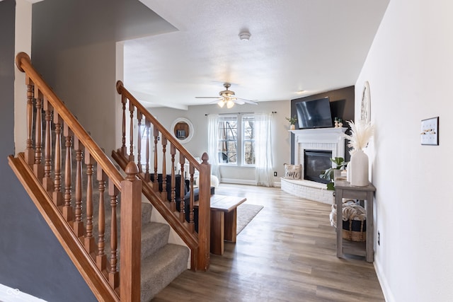 staircase with ceiling fan, a fireplace, baseboards, and wood finished floors