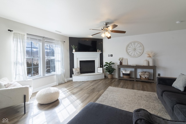 living area featuring a brick fireplace, baseboards, a ceiling fan, and wood finished floors