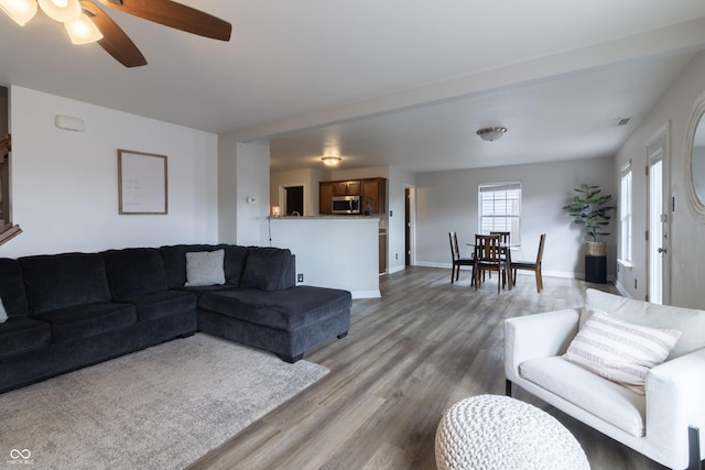 living room with a ceiling fan, visible vents, baseboards, and wood finished floors