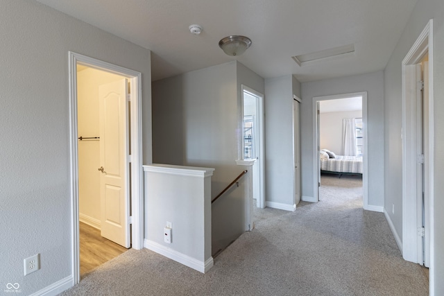 hallway featuring attic access, baseboards, light colored carpet, and an upstairs landing