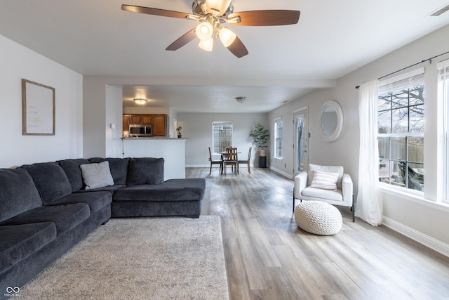 living room featuring light wood-style flooring, visible vents, ceiling fan, and baseboards