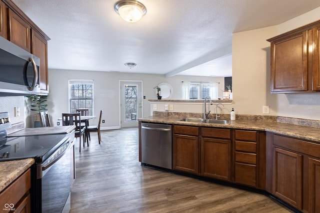 kitchen featuring stainless steel appliances, dark wood-type flooring, a sink, a peninsula, and baseboards