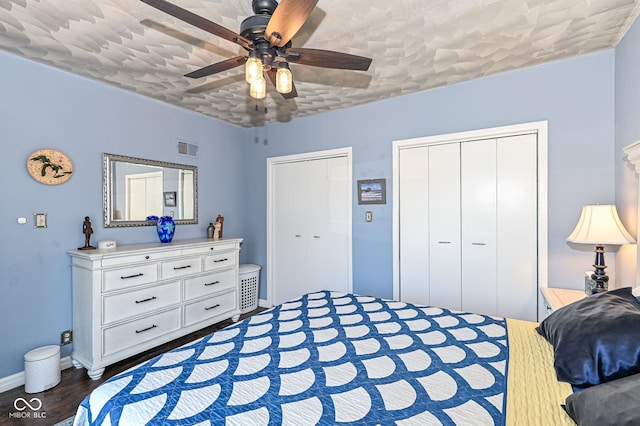 bedroom featuring visible vents, multiple closets, wood finished floors, baseboards, and ceiling fan