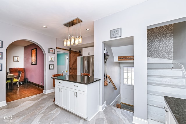 kitchen with arched walkways, hanging light fixtures, white cabinetry, a barn door, and stainless steel fridge