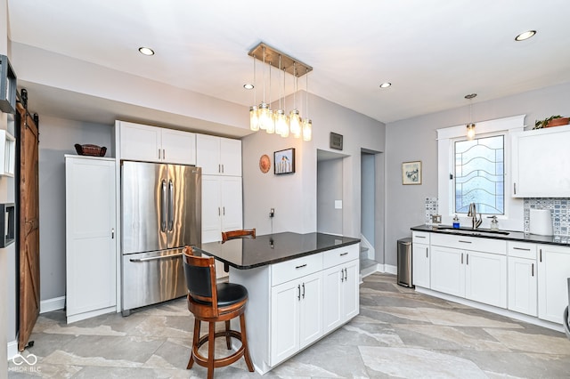 kitchen with dark countertops, white cabinets, hanging light fixtures, stainless steel fridge, and a sink