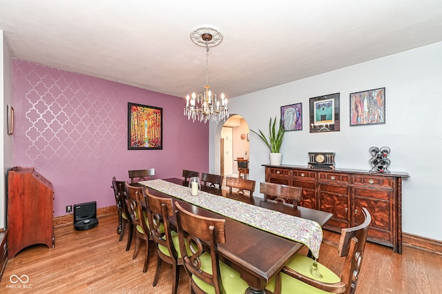 dining area featuring arched walkways, an inviting chandelier, light wood finished floors, and baseboards