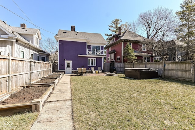 back of property with a garden, a lawn, a fenced backyard, and a hot tub