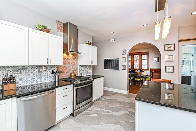 kitchen with visible vents, arched walkways, appliances with stainless steel finishes, wall chimney exhaust hood, and backsplash