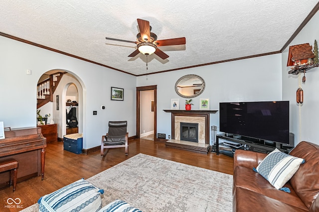 living area featuring a ceiling fan, a textured ceiling, wood finished floors, arched walkways, and a premium fireplace