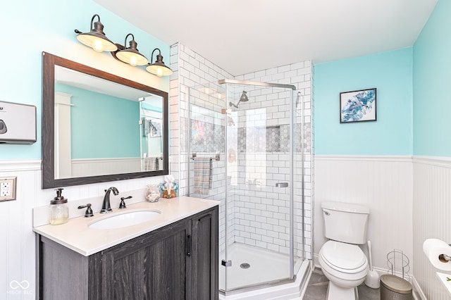 bathroom featuring a wainscoted wall, a stall shower, toilet, and vanity