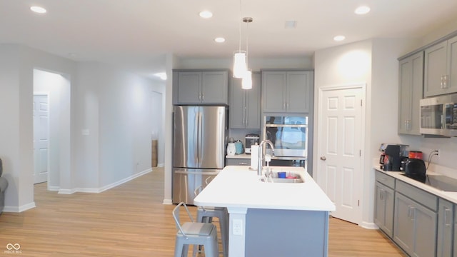 kitchen featuring stainless steel appliances, sink, decorative light fixtures, and an island with sink