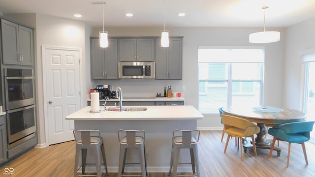 kitchen with sink, decorative light fixtures, a center island with sink, appliances with stainless steel finishes, and gray cabinets