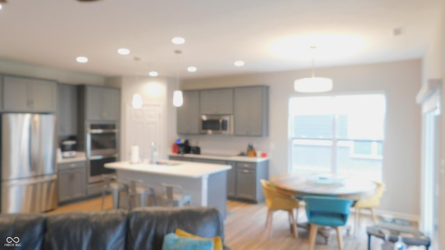 kitchen featuring appliances with stainless steel finishes, sink, gray cabinetry, hanging light fixtures, and a center island with sink