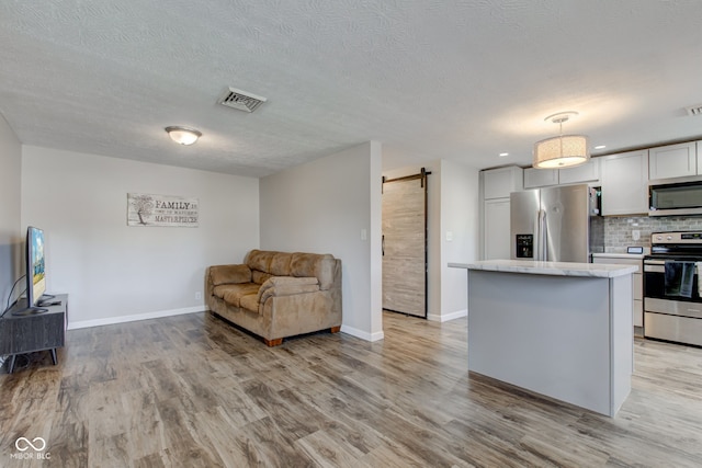 kitchen with light hardwood / wood-style flooring, hanging light fixtures, stainless steel appliances, a barn door, and backsplash