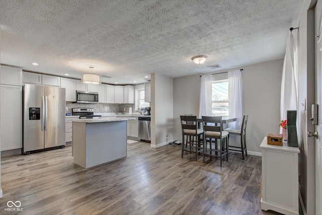 kitchen featuring tasteful backsplash, white cabinetry, pendant lighting, stainless steel appliances, and hardwood / wood-style floors