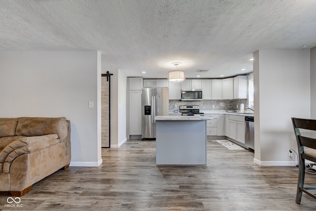 kitchen with a center island, light hardwood / wood-style flooring, pendant lighting, stainless steel appliances, and a barn door