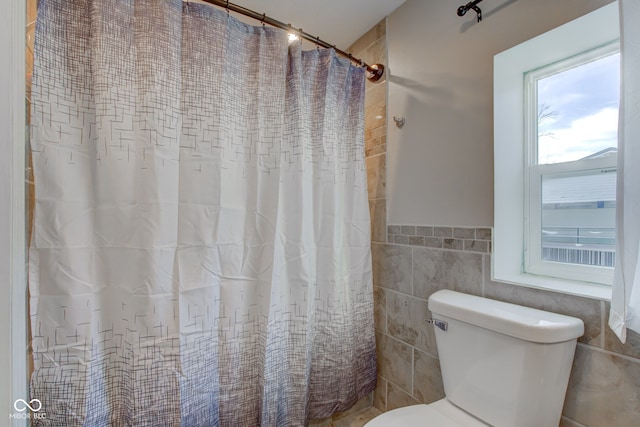 bathroom featuring walk in shower, toilet, and tile walls