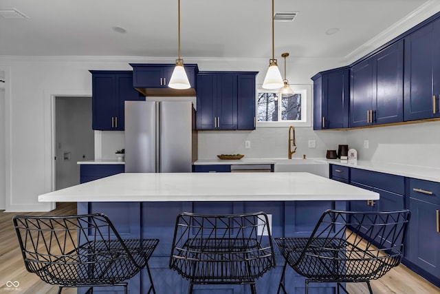 kitchen with blue cabinetry, a breakfast bar area, decorative light fixtures, stainless steel fridge, and a kitchen island