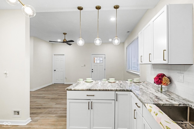 kitchen with white cabinetry, hanging light fixtures, decorative backsplash, and light hardwood / wood-style flooring