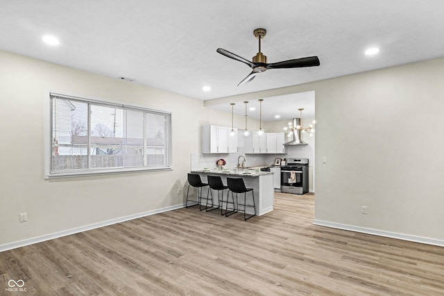 kitchen featuring stainless steel stove, a breakfast bar area, white cabinetry, kitchen peninsula, and wall chimney exhaust hood