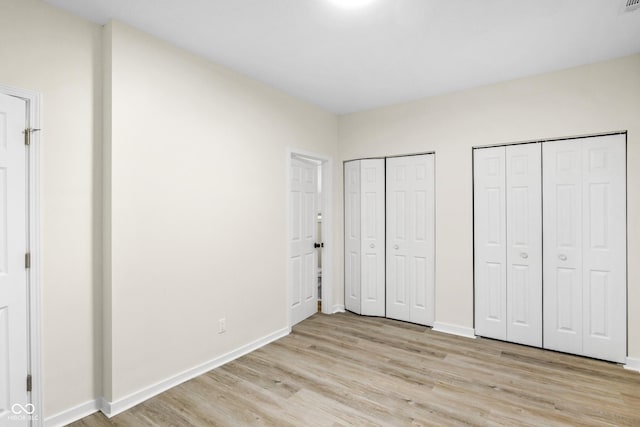 unfurnished bedroom featuring two closets and light hardwood / wood-style flooring