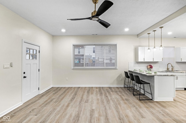 kitchen with a breakfast bar, white cabinetry, light wood-type flooring, pendant lighting, and backsplash