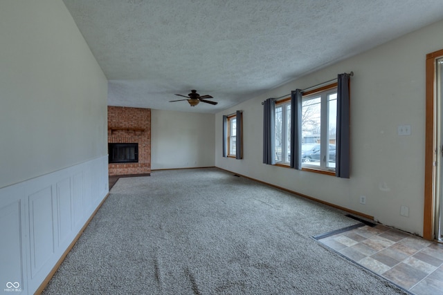 unfurnished living room featuring ceiling fan, light colored carpet, a textured ceiling, and a fireplace