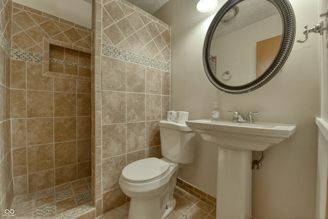 bathroom with tiled shower, tile patterned floors, a textured ceiling, and toilet