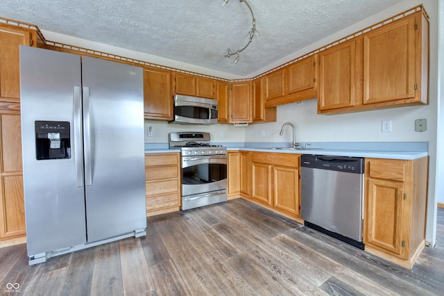 kitchen featuring sink, rail lighting, stainless steel appliances, a textured ceiling, and dark hardwood / wood-style flooring