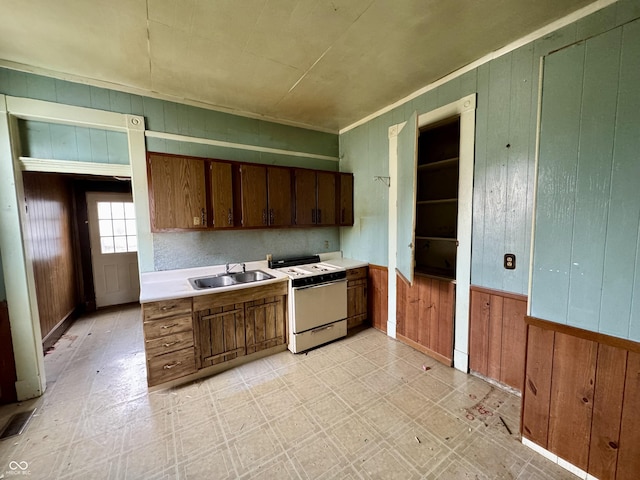 kitchen featuring white range oven, sink, and wood walls