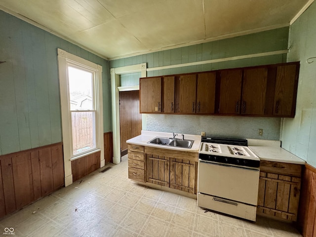 kitchen with sink, white range with gas stovetop, and wooden walls